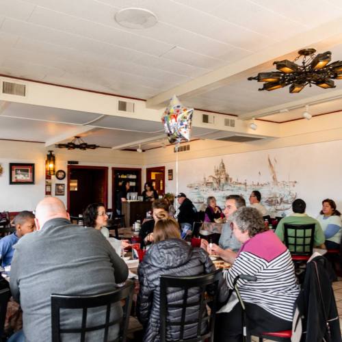 A busy restaurant interior with diners at tables, featuring a mural and decorative lighting.