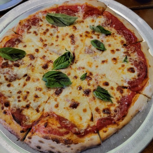A freshly baked pizza topped with melted cheese and fresh basil leaves, served on a silver platter.