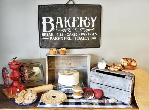A rustic bakery display featuring bread, pastries, cookies, and a sign reading "Bakery" with vintage decor.