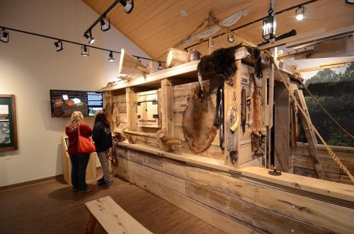 Two visitors explore a wooden exhibit featuring historical artifacts and displays in a museum setting.