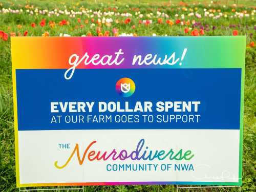 Sign in a flower field announcing that every dollar spent at the farm supports the Neurodiverse Community of NWA.