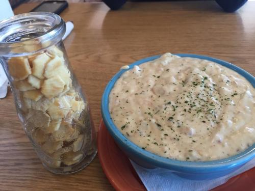 A bowl of creamy soup topped with herbs, next to a glass jar filled with crackers on a wooden table.