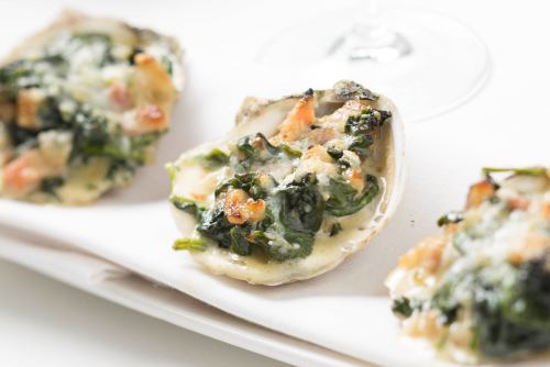 Baked oysters topped with spinach and cheese, served on a white plate.