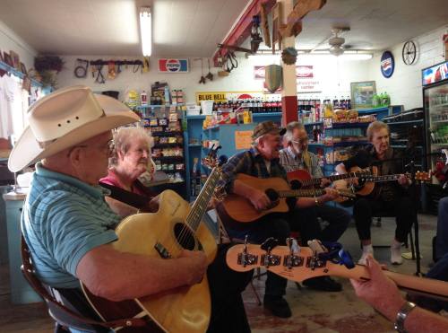 A group of musicians playing guitars in a cozy store, with shelves of snacks and drinks in the background.