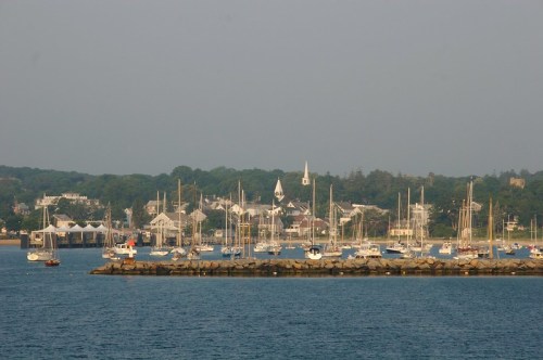 A serene harbor scene with sailboats docked and a coastal town in the background under a clear sky.