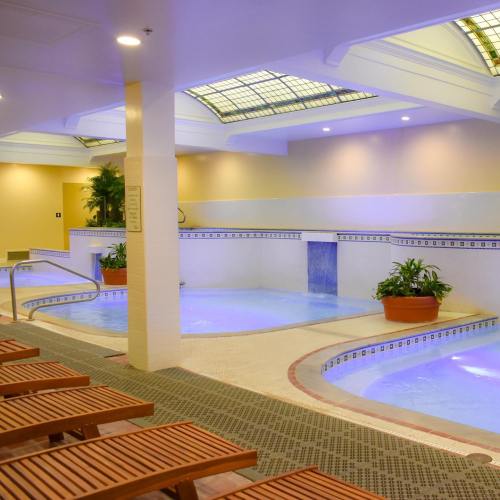 Indoor pool area with lounge chairs, plants, and soft blue lighting. Relaxing atmosphere with a modern design.