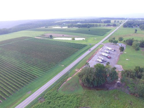Aerial view of a rural landscape with vineyards, a road, and a parking area surrounded by greenery.