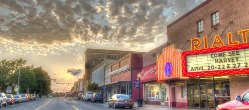 A street view of the Rialto Theatre with a colorful marquee, shops, and a dramatic sky at sunset.