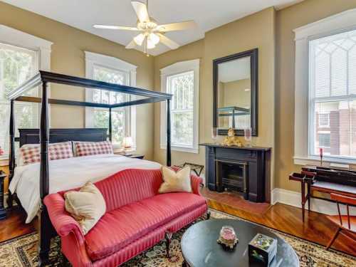 Cozy bedroom with a four-poster bed, red sofa, fireplace, and large windows letting in natural light.