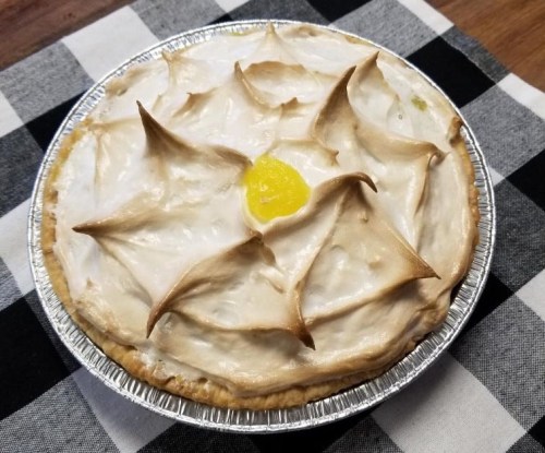 A lemon meringue pie with a golden center and decorative peaks, placed on a black and white checkered cloth.