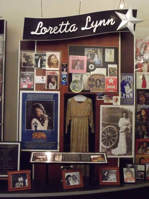 Display dedicated to Loretta Lynn, featuring photos, memorabilia, and a dress, highlighting her musical legacy.