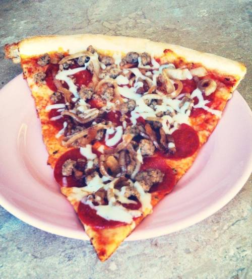 A slice of pizza topped with pepperoni, sausage, onions, and melted cheese on a pink plate.