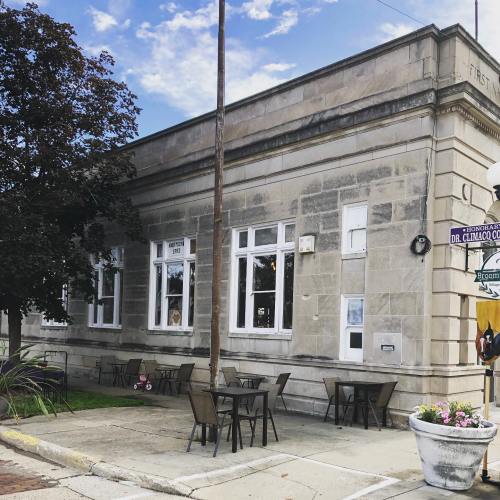 A historic building with large windows, outdoor seating, and a blue sky in the background.