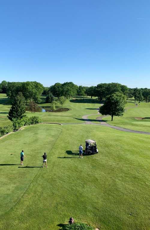 A sunny golf course scene with three golfers near a cart, surrounded by lush greenery and a pond in the background.