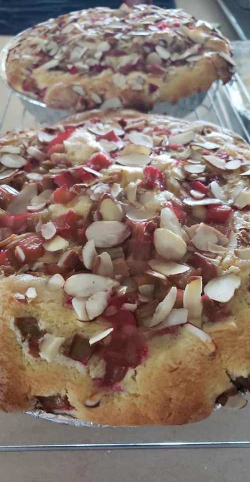 Two freshly baked cakes topped with sliced almonds and rhubarb, cooling on a wire rack.