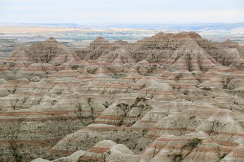 A panoramic view of layered, colorful rock formations in a rugged landscape under a cloudy sky.