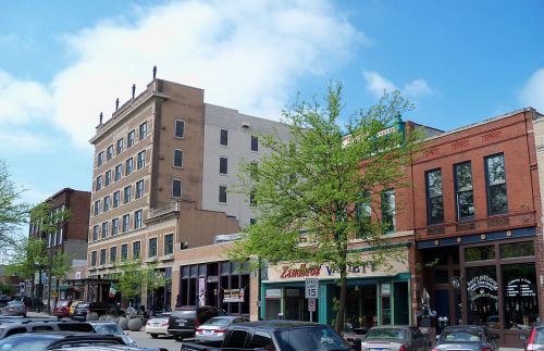 A vibrant downtown street with shops, trees, and a historic building under a blue sky.