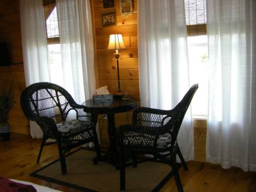 Cozy interior with two wicker chairs and a small table by a window, surrounded by light curtains and wooden walls.