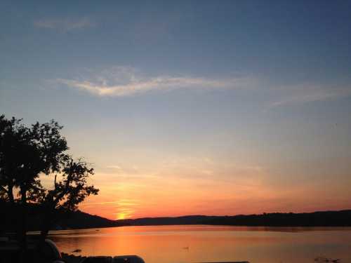 A serene sunset over a calm lake, with silhouettes of trees and hills against a colorful sky.