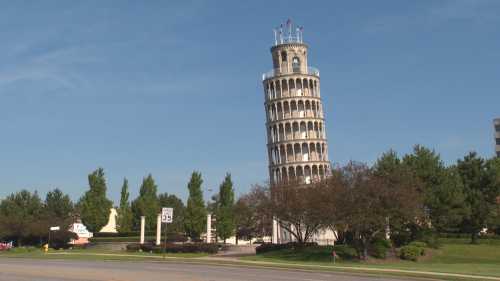 A leaning tower resembling the Leaning Tower of Pisa, surrounded by trees and a clear blue sky.