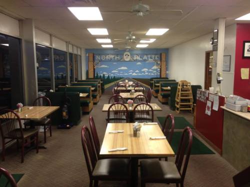 Interior of a restaurant with wooden tables, chairs, and a mural of a landscape on the back wall.