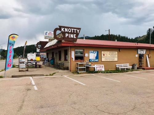 A rustic building with a sign reading "Knotty Pine," featuring outdoor seating and signs for ice cream and fishing supplies.