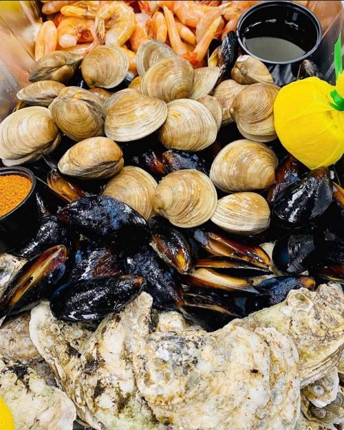 A seafood platter featuring clams, mussels, oysters, shrimp, and dipping sauces, garnished with lemon.