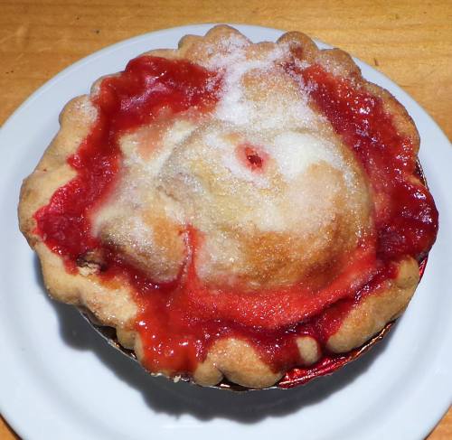 A freshly baked cherry pie with a golden crust and red filling, sitting on a white plate.