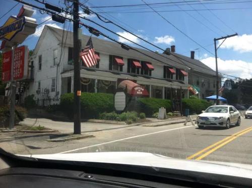 A restaurant with red awnings and an American flag, set on a street with power lines and a car passing by.