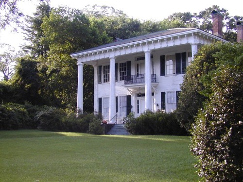 A large white house with columns, surrounded by greenery and a well-maintained lawn.