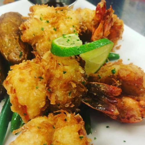 Crispy fried shrimp garnished with lime and herbs, served with green beans and a dipping sauce on a white plate.