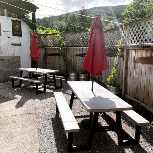 Outdoor seating area with picnic tables and red umbrellas, surrounded by greenery and mountains in the background.