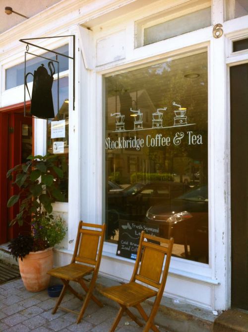 A cozy coffee shop window with a sign for "Stockbridge Coffee & Tea" and two wooden chairs outside.