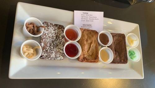 A platter with three dessert squares and various colorful sauces in small cups, accompanied by a menu card.