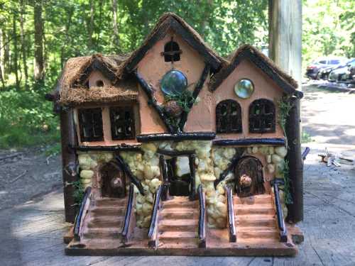 A whimsical miniature house made of natural materials, featuring stairs, windows, and decorative stones, set in a forest.