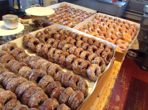 A variety of freshly made donuts arranged on trays, featuring glazed and powdered sugar toppings.