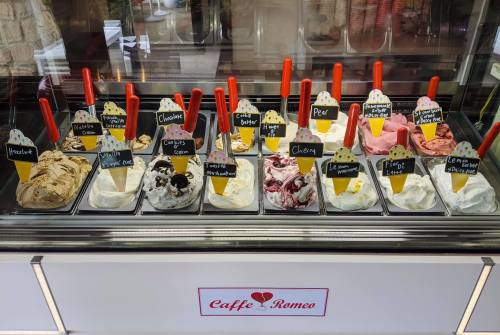 A display of various ice cream flavors in a shop, each labeled with a small sign, featuring colorful scoops in containers.