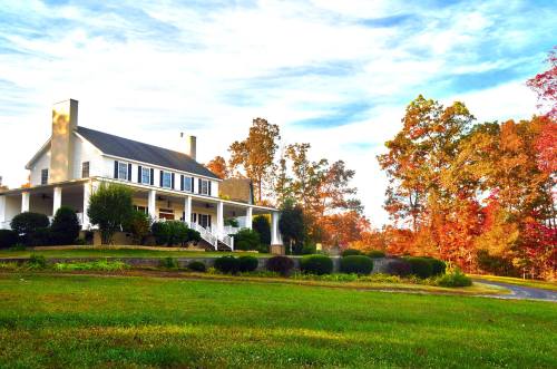 A charming white house with a porch, surrounded by colorful autumn trees and a green lawn under a blue sky.