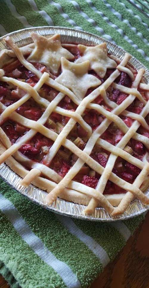 A freshly baked pie with a lattice crust and star-shaped cutouts, resting on a green striped cloth.