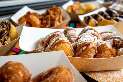 A variety of sweet pastries, including doughnuts and caramel-covered treats, displayed in paper trays.