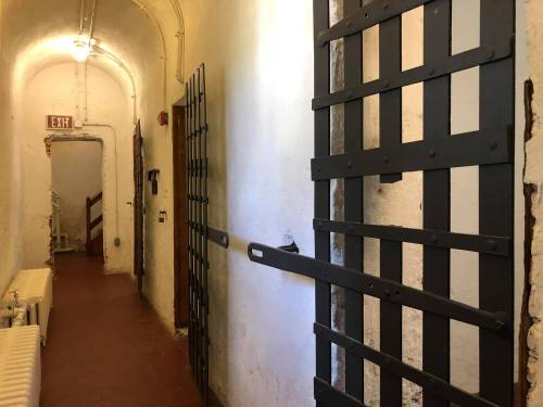 A dimly lit hallway with two heavy metal doors and a staircase at the end, featuring exposed brick walls.