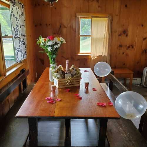 A cozy wooden room with a table set for a gathering, featuring flowers, candles, and decorative balloons.