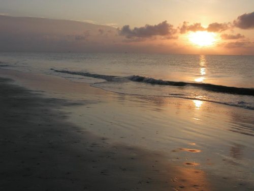 A serene beach at sunset, with gentle waves lapping at the shore and a colorful sky reflecting on the water.
