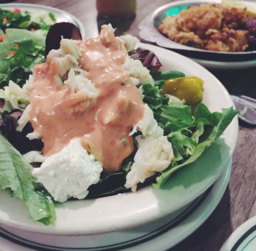 A fresh salad with greens, crab meat, and a creamy dressing, served in a white bowl.