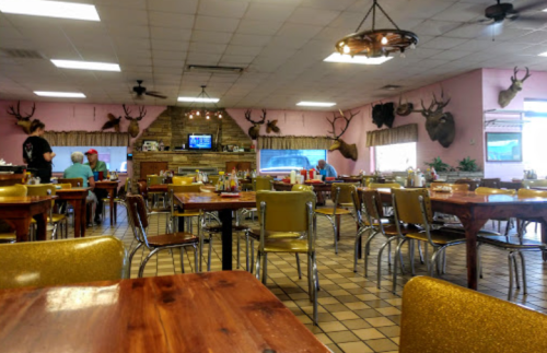 A cozy restaurant interior with wooden tables, metal chairs, and mounted deer heads on the walls.