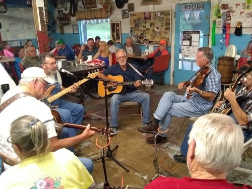 A group of musicians playing bluegrass music in a cozy venue, with an audience enjoying the performance in the background.