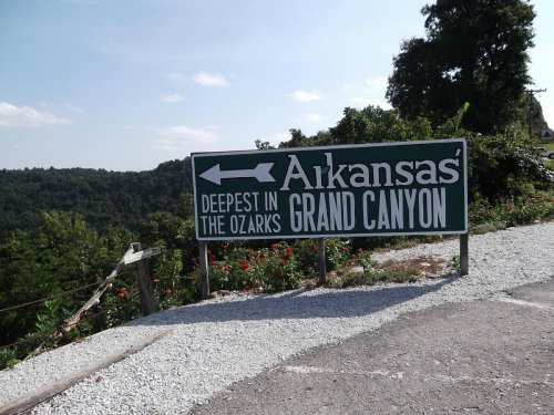 Sign for "Arkansas Grand Canyon" with directions, stating it's the "Deepest in the Ozarks," surrounded by greenery.