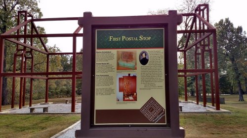 Sign about the First Postal Stop, featuring historical information and images, with a partially constructed structure in the background.