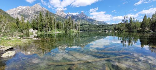 A serene lake surrounded by mountains and trees, with clear reflections on the water's surface.