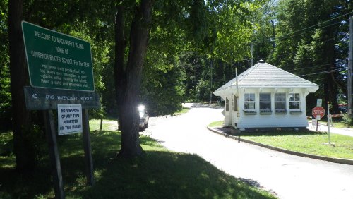 A sign welcomes visitors to Woodworth Island, featuring a small white building and a stop sign along a tree-lined road.